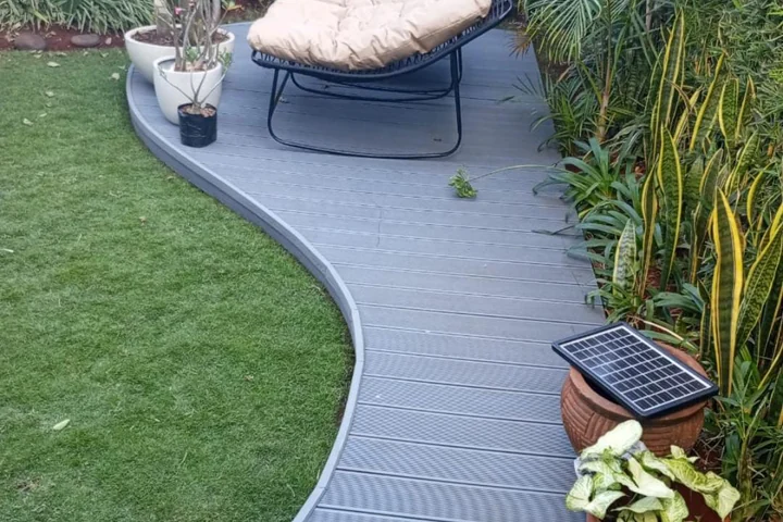 Curved grey WPC walkway running between a lawn and a planted border