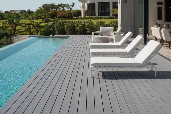 Grey composite decking running the length of an infinity pool with sun loungers